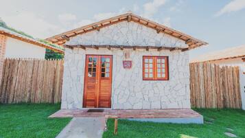 Una casa de piedra con puerta y ventanas de madera, rodeada por una cerca de bambú.