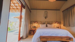 A bedroom with a stone wall, a wooden bed with a bench, a small stool, and a view of a swimming pool. - VILAGOA POUSADA (Coqueiro Seco)