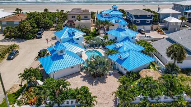 Zona residencial costera con varias casas de techos azules, una piscina central y una playa al fondo.