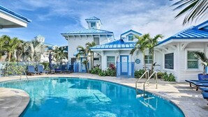Un área de piscina con una piscina azul cristalina, sillas de descanso y un edificio de techo azul y paredes blancas.