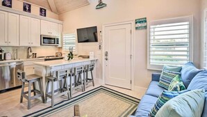 Una cocina moderna con armarios blancos, un microondas y una zona de bar con taburetes. Hay un televisor sobre la encimera y un letrero en la puerta.