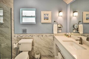 Une salle de bain moderne avec des toilettes, un lavabo et un grand miroir. Des tableaux encadrés ornent le mur, et une fenêtre se trouve au-dessus du lavabo.