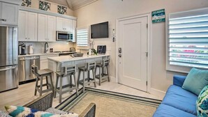 A kitchen with white cabinets, a central island with stools, a microwave, and a television above the island. - Beachside Studio w/ Pool Access (New Smyrna Beach)