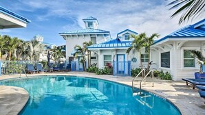 A swimming pool surrounded by buildings with blue roofs and white walls, palm trees, and lounge chairs. - Beachside Studio w/ Pool Access (New Smyrna Beach)