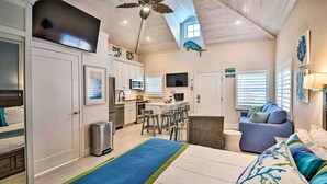 A compact, well-lit room with a bed, a seating area, a kitchenette, and a ceiling fan. - Beachside Studio w/ Pool Access (New Smyrna Beach)