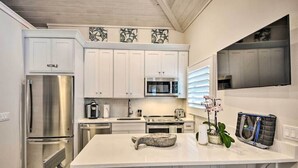 A modern kitchen with white cabinetry, stainless steel appliances, a large island, and a flat-screen TV mounted above the island. - Beachside Studio w/ Pool Access (New Smyrna Beach)