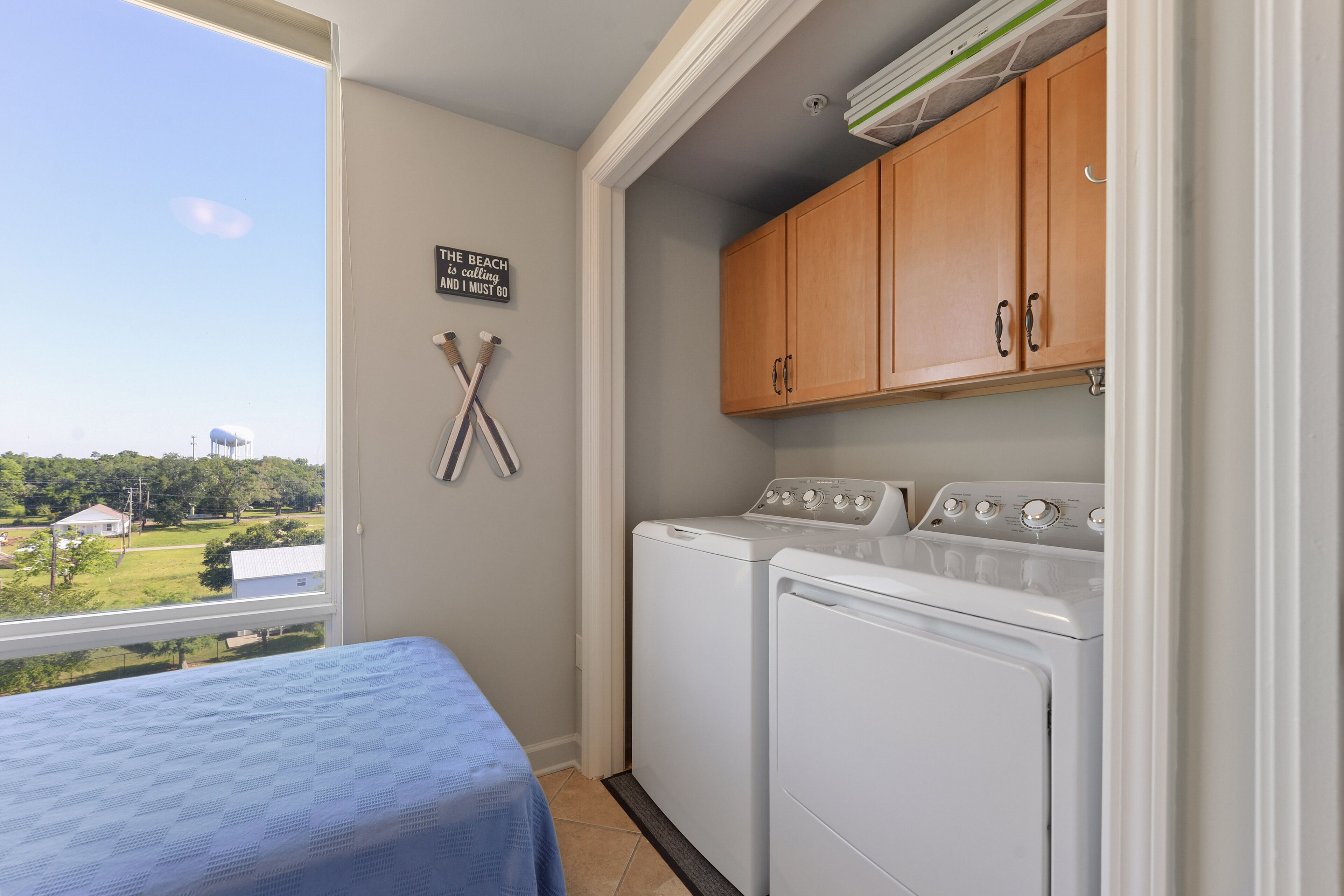 A laundry room with two washing machines, wooden cabinets, and a view of the outdoors.