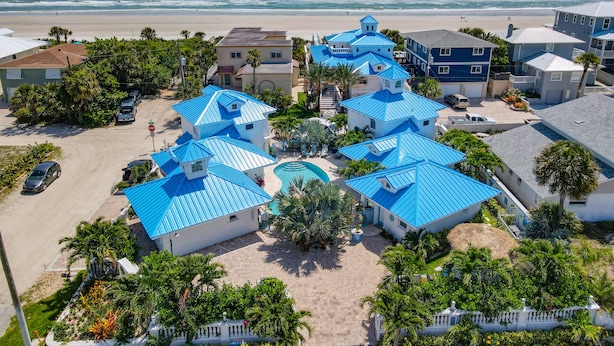 A coastal residential area with multiple houses featuring blue roofs, a central swimming pool, and a beach in the background.