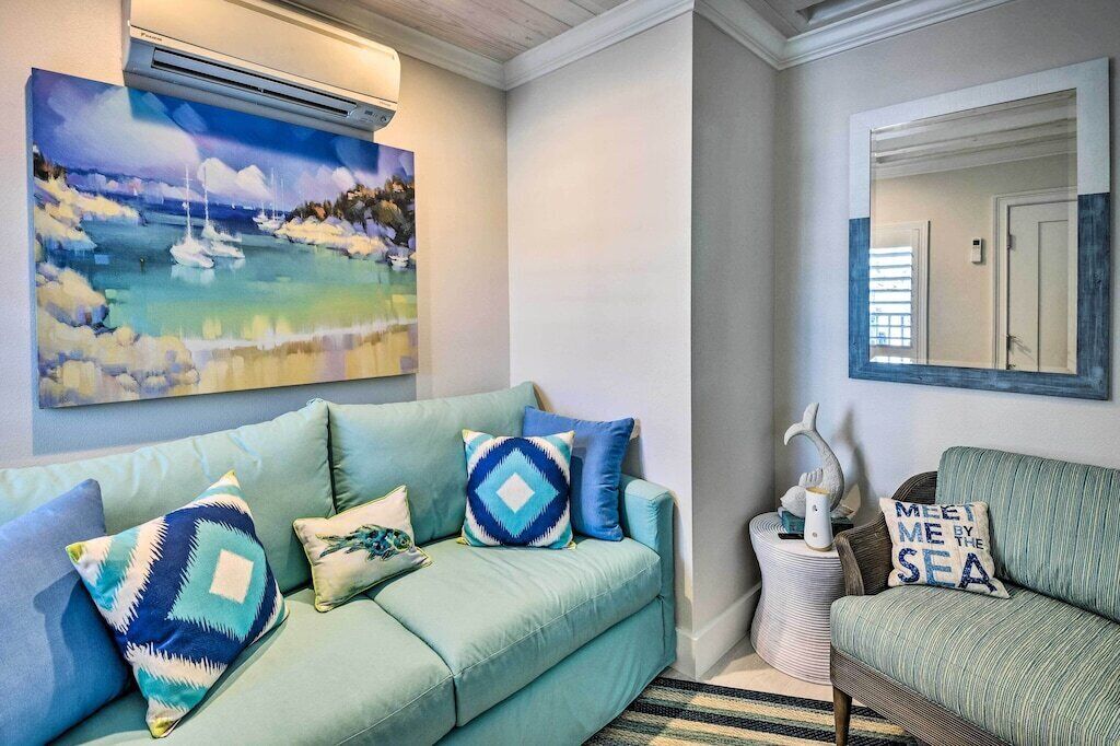 Una sala de estar con un sofá color turquesa, un cuadro de una escena costera y un espejo que refleja una puerta.
