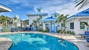 A pool area with a clear blue pool, lounge chairs, and a building with a blue roof.