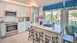 A modern kitchen with white cabinets, stainless steel appliances, and a bar area with stools.