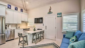 Una cocina moderna con armarios blancos, una isla central con taburetes altos, un televisor de pantalla plana y un letrero que dice "The Beach is my happy place".