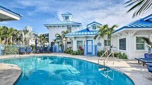 Ett poolområde med en klarblå pool, solstolar och en byggnad med ett blått tak och vita väggar.