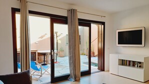 A living room with a sofa, a coffee table, a flat-screen TV, and a sliding glass door leading to an outdoor patio with a table and chairs. - Fantastic view, maximum relax and wellness. (Costa Paradiso)