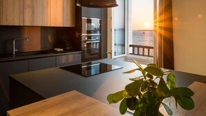 Una cocina moderna con una isla central, una lámpara colgante y vistas al mar a través de amplios ventanales.