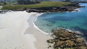 Une plage côtière aux eaux limpides, bordée d’un rivage sablonneux et ponctuée de formations rocheuses.