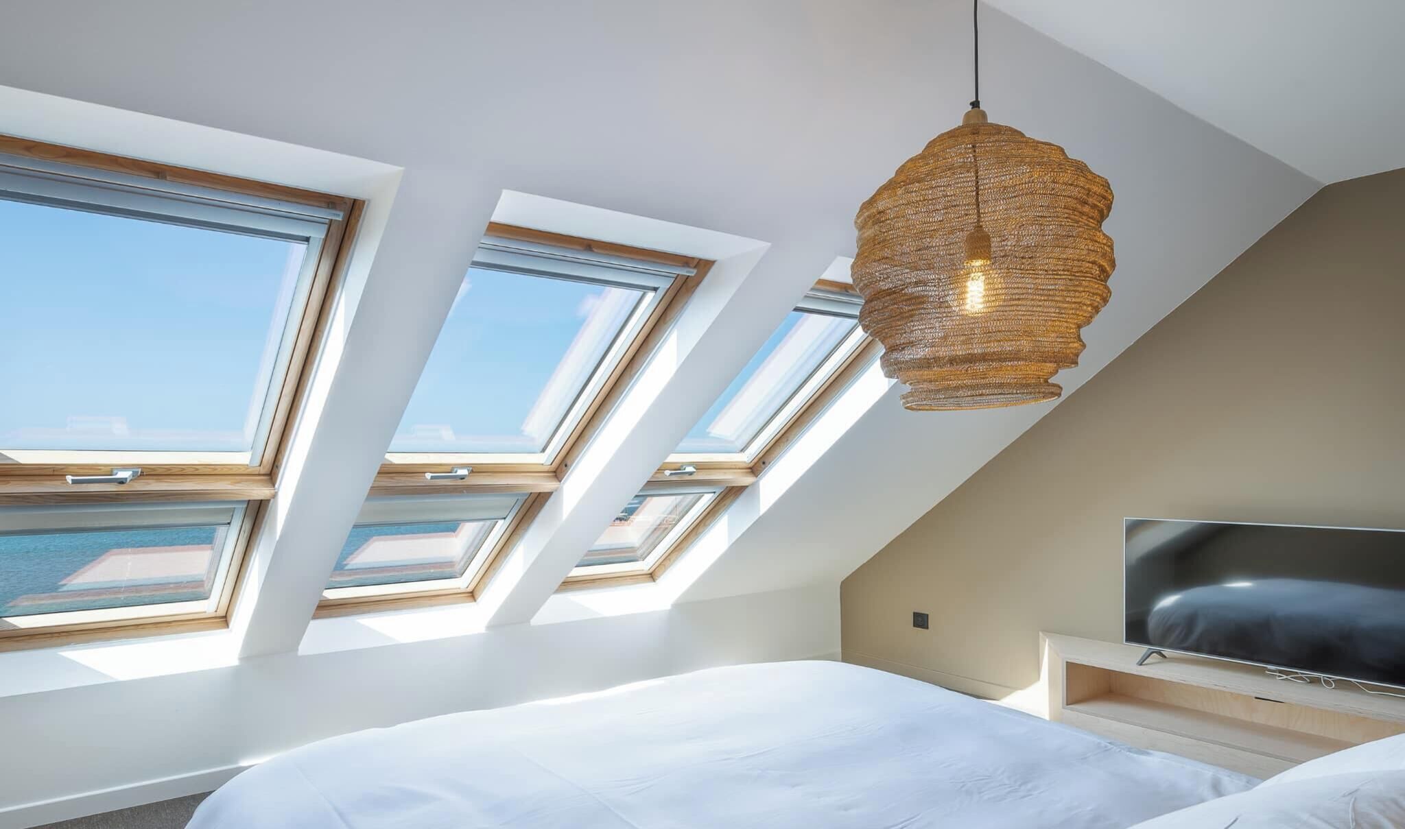 A bedroom with skylights, a bed, a TV, and a hanging light fixture.