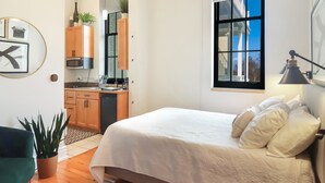 Een moderne slaapkamer met een groot bed, uitzicht, een keukenhoek en een plant in pot.