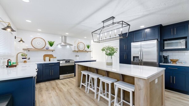 A modern kitchen with dark blue cabinets, a stainless steel refrigerator, a gas stove, and a central island with bar stools. - Updated Eagle Home | Hot Tub + Walk to Downtown (Eagle)