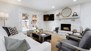 A modern living room with a fireplace, a television mounted on the wall, and a comfortable seating area with a sofa and chairs. - Updated Eagle Home | Hot Tub + Walk to Downtown (Eagle)