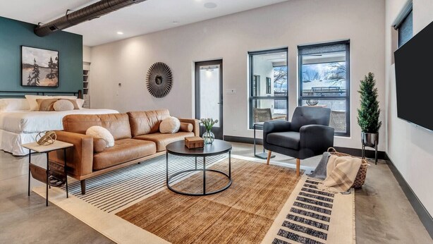 Een moderne woonkamer met een bank, fauteuil, salontafel en een groot raam met uitzicht op de omgeving.