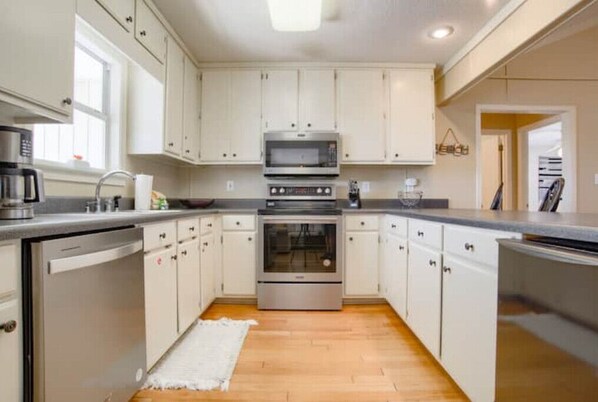 Kitchen features an oven, microwave, and dishwasher, with a window and light-colored wood floor.