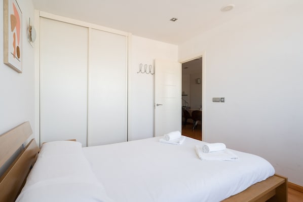 Ein Schlafzimmer mit einem Bett, einem Holzkopfende, einem Kleiderschrank und einem durch eine offene Tür einsehbaren Badezimmer.