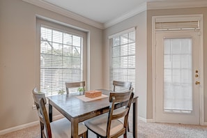 A dining area with a table and four chairs, a window with blinds, and a door with a window.