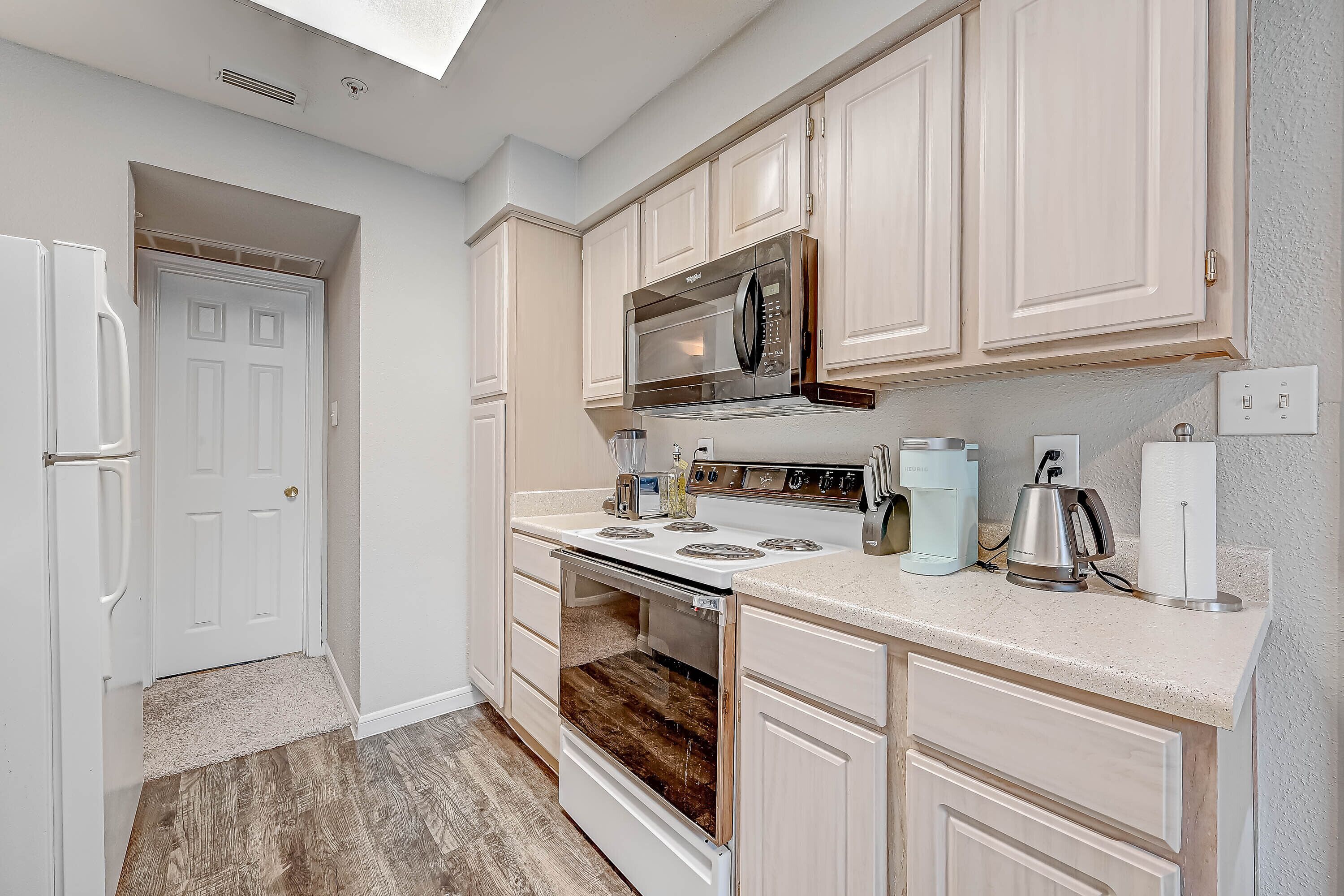 A kitchen with white cabinets, a stainless steel microwave, a stove, and a coffee maker.