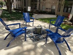 Outdoor seating with blue chairs arranged around a stone fire pit.