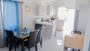 Una cocina moderna con armarios blancos, un comedor con mesa de mármol y un pequeño espacio de trabajo.