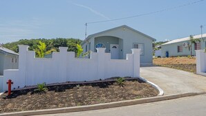Un barrio residencial con una casa que tiene valla de piquetes blancos, un pequeño jardín y un camino de entrada pavimentado.