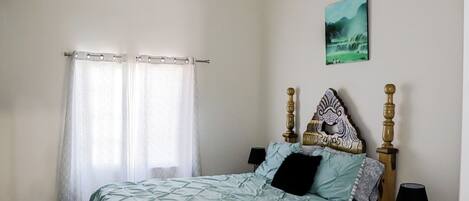 Une chambre à coucher avec un lit, des rideaux, une tête de lit, des lampes de chevet et un tableau au mur.