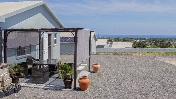 Un espacio de estar al aire libre techado con una mesa, sillas, plantas en macetas y vistas al mar.