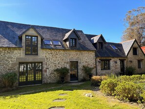 Una casa in pietra con tetto spiovente, diverse finestre e un giardino curato con lastre di pietra.