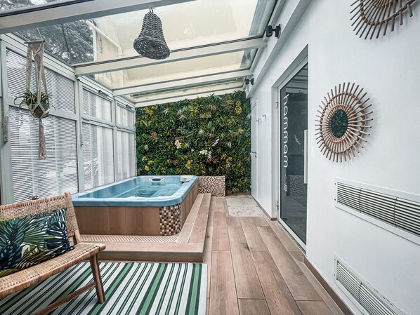 Relax in a serene outdoor space with a wicker sofa, hot tub, and lush green wall.