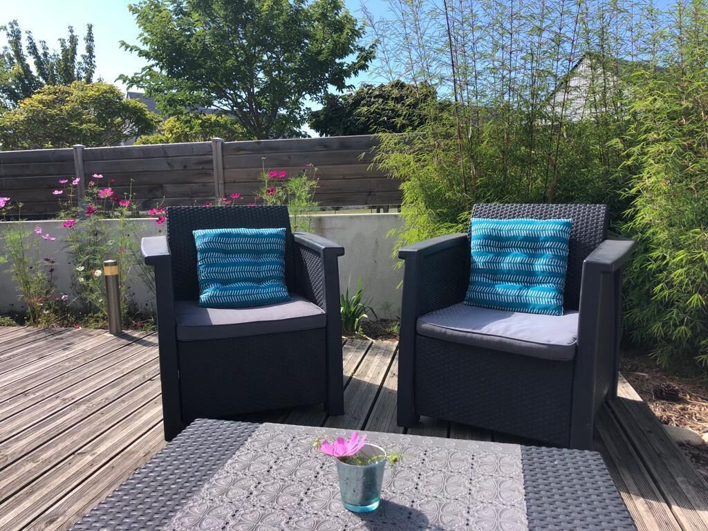 Twee buitenwicker stoelen met patroon kussens, een bijzettafeltje met een decoratieve vaas, en een houten terras.