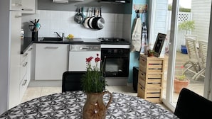 Une cuisine compacte avec des meubles blancs, une cuisinière noire et un porte-casseroles suspendu.