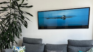 Un salon moderne avec un canapé gris, une table basse en verre et un grand tableau représentant un paysage.