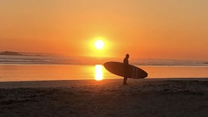 Une personne tenant une planche de surf sur une plage au coucher du soleil.