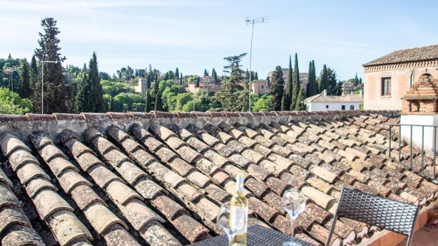 A terrace with a table set for two, overlooking a cityscape with historic buildings and trees.