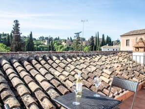 Een terras met een tafel voor twee, met uitzicht op een stadsgezicht met historische gebouwen en bomen.