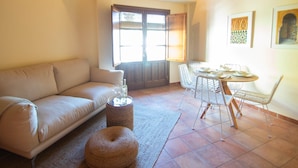A living room with a sofa, a round table with chairs, a small rug, and a decorative stool.