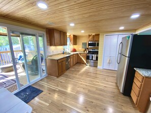 A spacious kitchen with wooden cabinets, a stainless steel refrigerator, and a large island. - Charming Beach Bungalow: 9 min walk to the Beach (Oak Island)