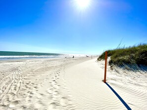 A sandy beach with footprints leading to the water, a clear sky, and a distant view of the ocean. - Charming Beach Bungalow: 9 min walk to the Beach (Oak Island)