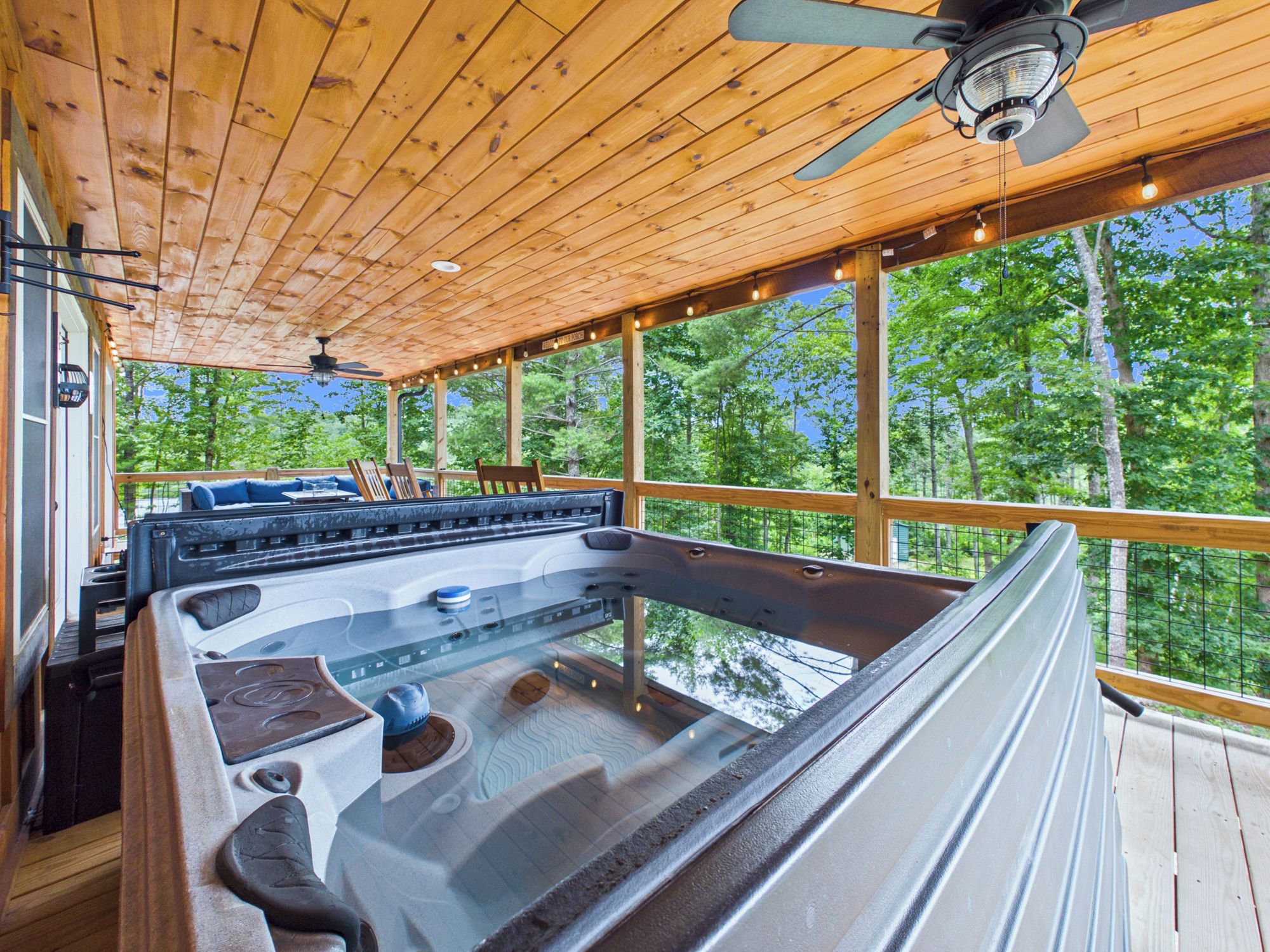 A hot tub area with wooden ceiling and large windows overlooking a forest.