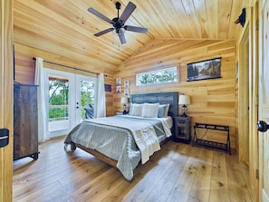 A wooden cabin bedroom with a bed, nightstands, a ceiling fan, and a window. - Pet-Friendly Cabin w/Mountain Views, Large Deck, Hot Tub & Fire Pit (Murphy)
