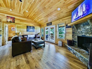 A log cabin interior with a fireplace, wooden floors, and a television.