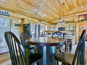 A wooden interior with a round dining table surrounded by chairs, a refrigerator, and a microwave.