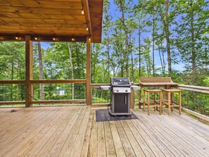 An outdoor deck with a grill and a table, surrounded by trees. - Pet-Friendly Cabin w/Mountain Views, Large Deck, Hot Tub & Fire Pit (Murphy)